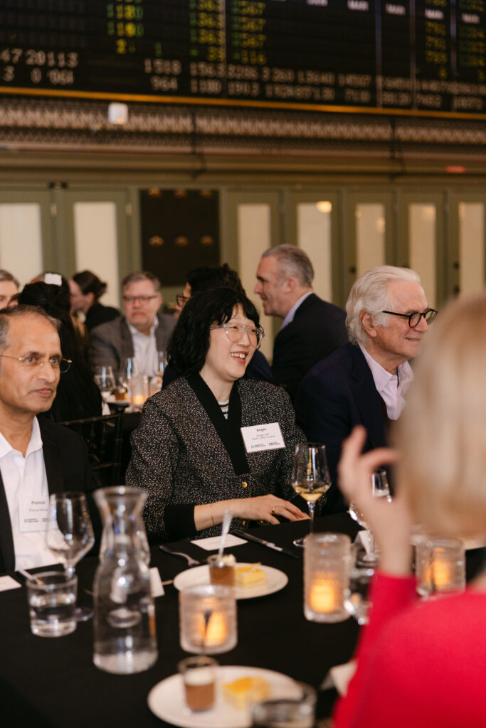 MPR corporate gala guests laughing and dining at black-draped tables under the historic Grain Exchange stock ticker board — Minneapolis corporate event photographer Mycah Bain Photography