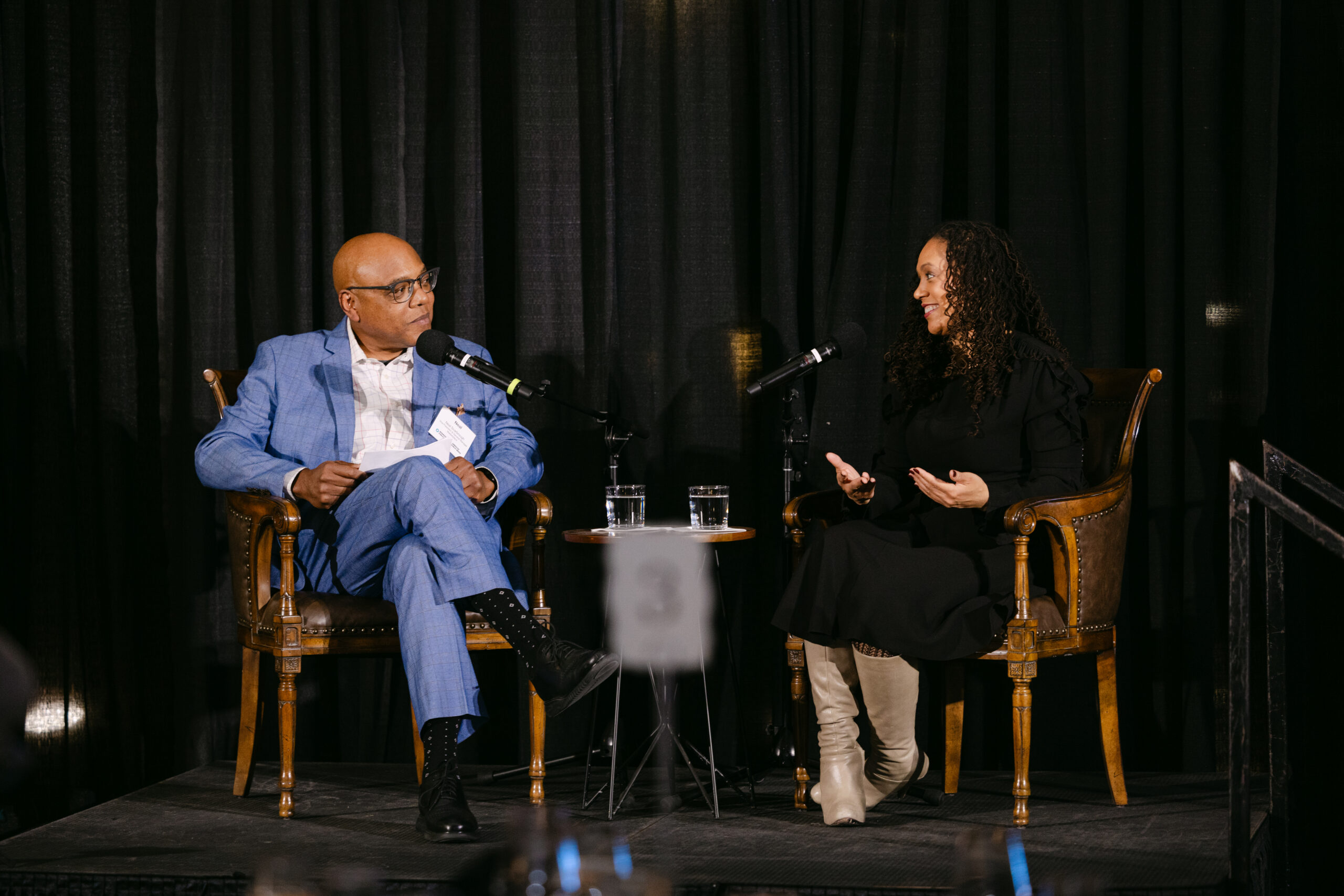 Two Minnesota Public Radio speakers in conversation on stage during MPR corporate event at the Minneapolis Grain Exchange photographed by Minneapolis corporate event photographer Mycah Bain Photography