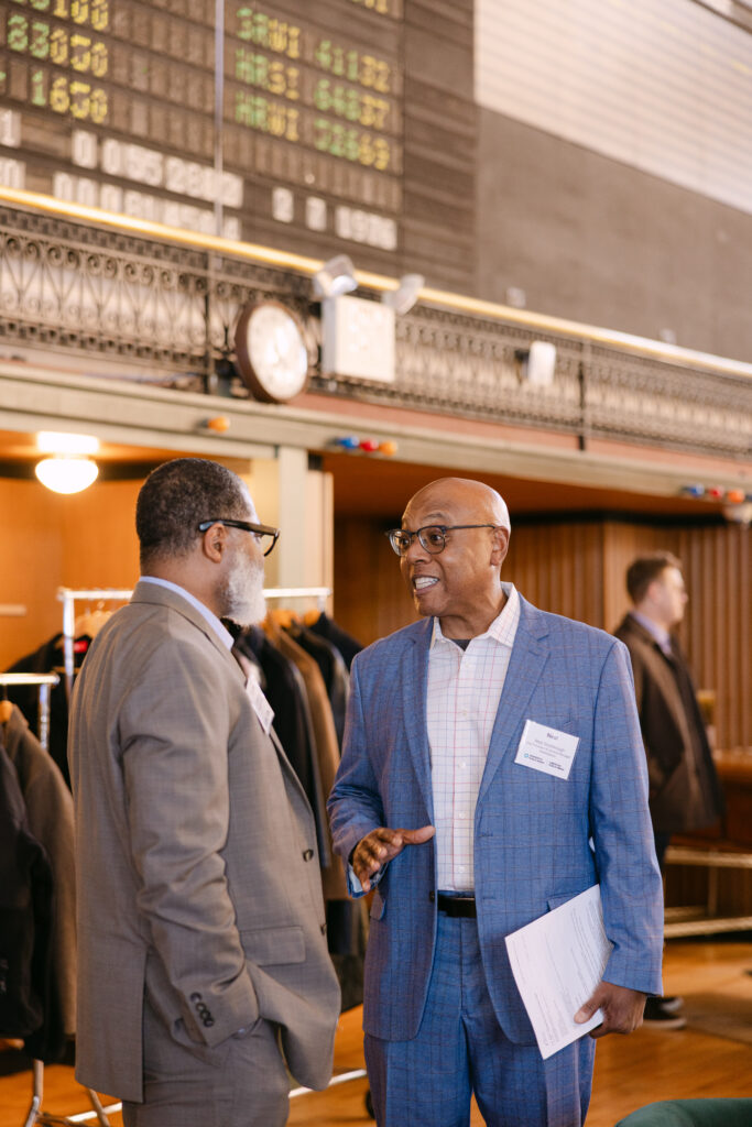 Two MPR corporate event guests in conversation in front of historic Grain Exchange stock ticker board — Minneapolis corporate event photographer Mycah Bain Photography