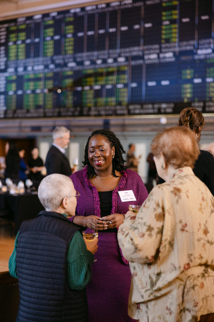 MPR corporate event guest in purple jacket networking and laughing in front of historic Minneapolis Grain Exchange stock ticker board — Mycah Bain Photography