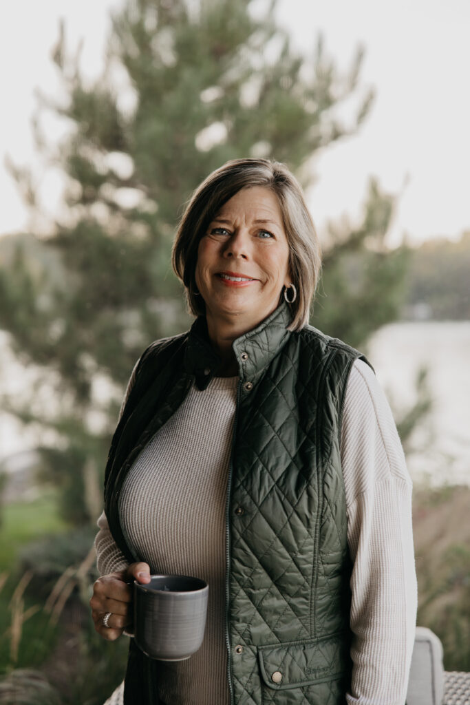 Dr. Melissa Polusny private practice therapist holding mug with lake view behind her — brand photography psychologist Minneapolis by Mycah Bain Photography