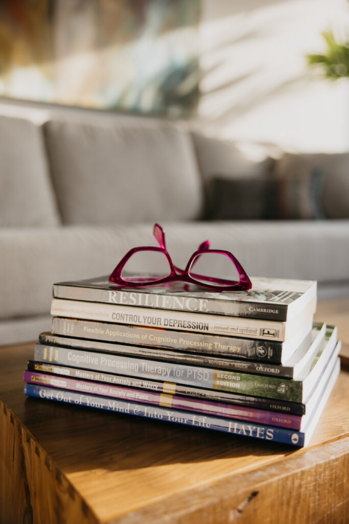 Stack of psychology and resilience books with red glasses on top — brand photography detail shot for Minneapolis private practice therapist