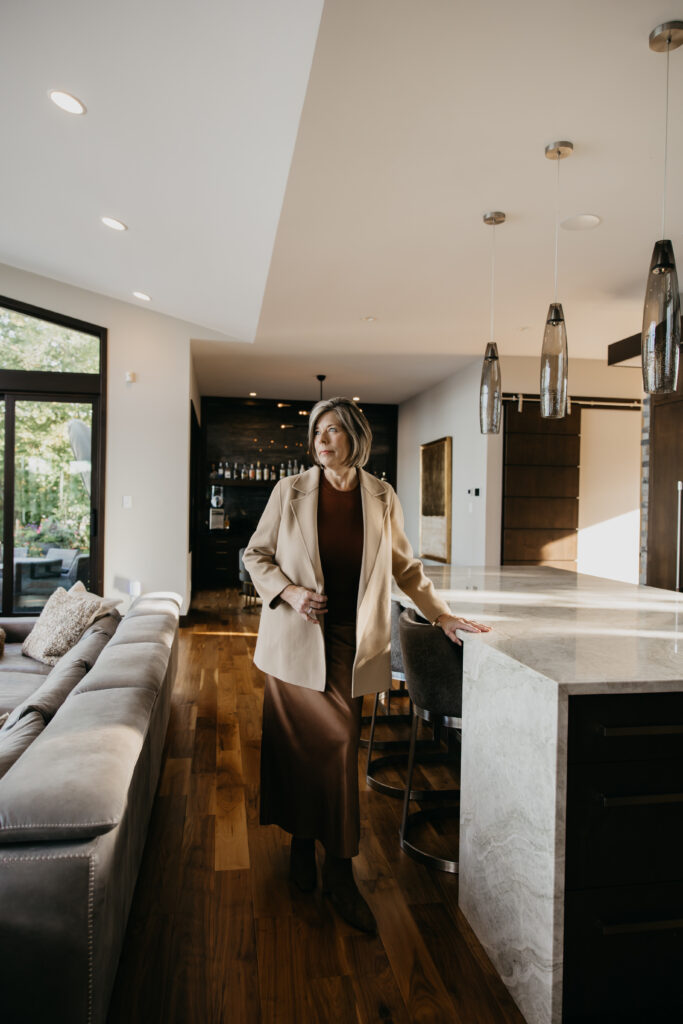 Dr. Melissa Polusny private practice psychologist standing at kitchen island in camel coat during brand photography psychologist Minneapolis session