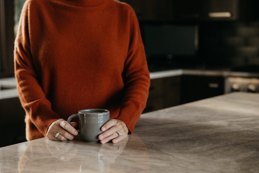 Close-up of Dr. Melissa Polusny holding grey coffee mug at marble counter — lifestyle B-roll from Minneapolis psychologist brand session