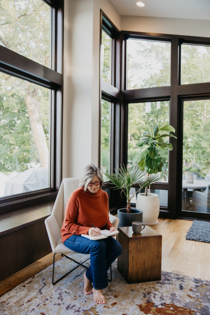 Dr. Melissa Polusny private practice therapist writing in chair by floor-to-ceiling windows during Minneapolis brand photography session