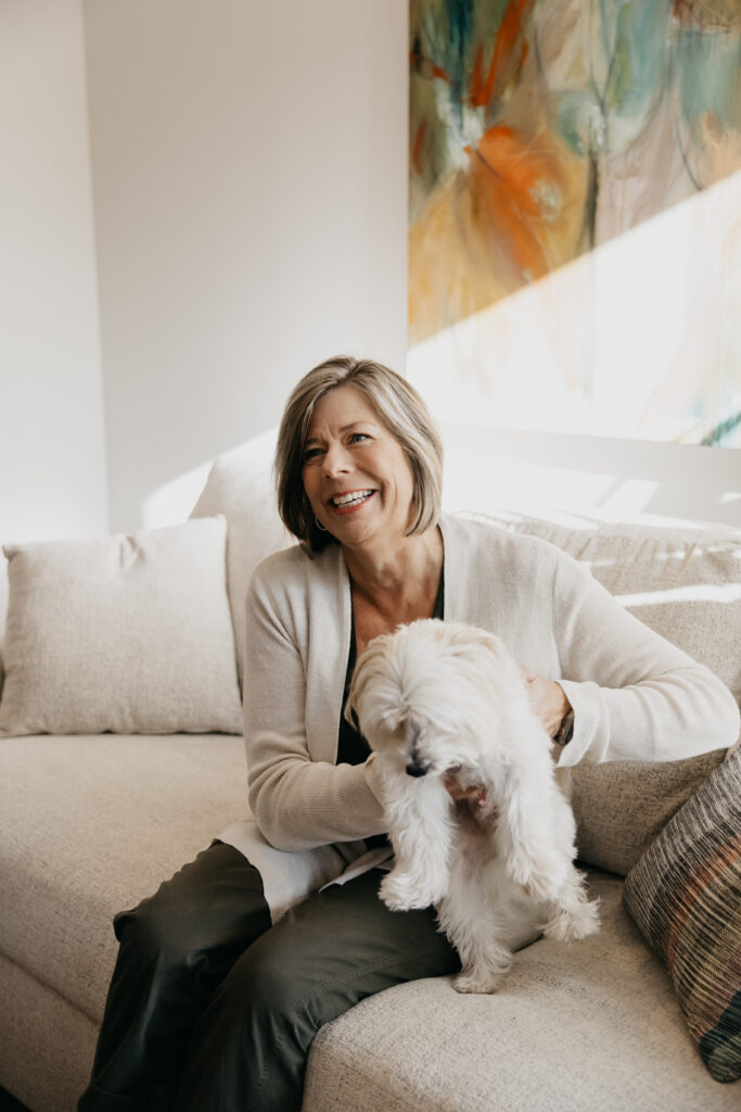 Dr. Melissa Polusny Minneapolis psychologist smiling with white dog on cream sofa during brand photography session