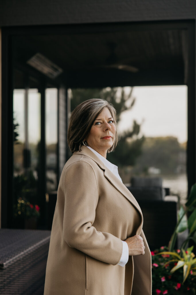 Dr. Melissa Polusny in camel coat standing on lakeside deck during brand photography psychologist Minneapolis session