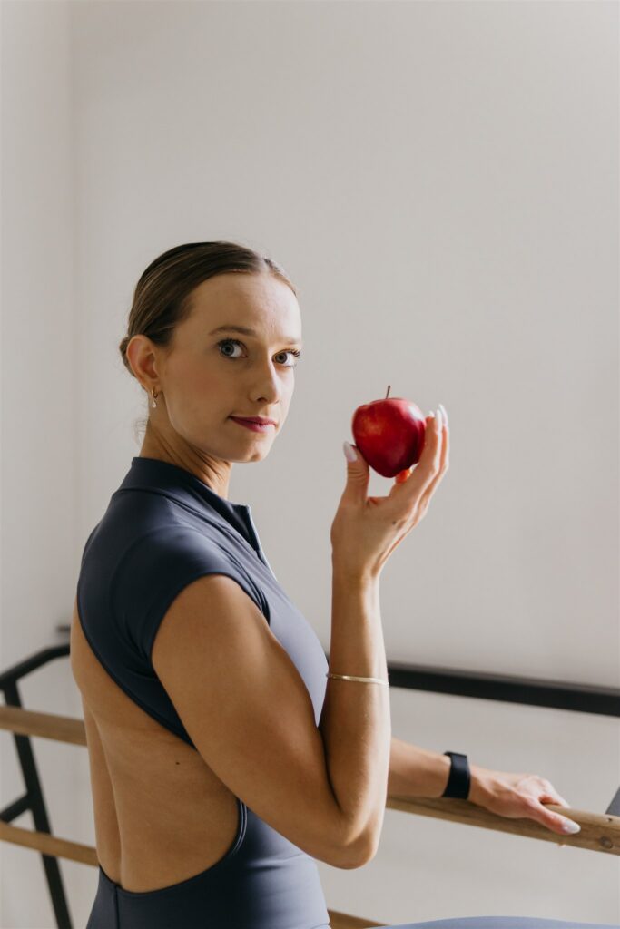 Lili Pfeifer of The Barbell Ballerina holding a red apple at the barre during nutrition coaching fitness brand photography Minneapolis session by Mycah Bain Photography