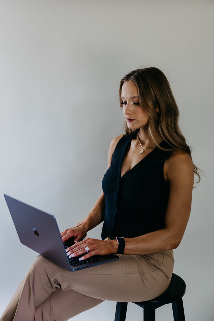 Lili Pfeifer of The Barbell Ballerina seated on stool with open laptop during fitness brand photography Minneapolis session by Mycah Bain Photography