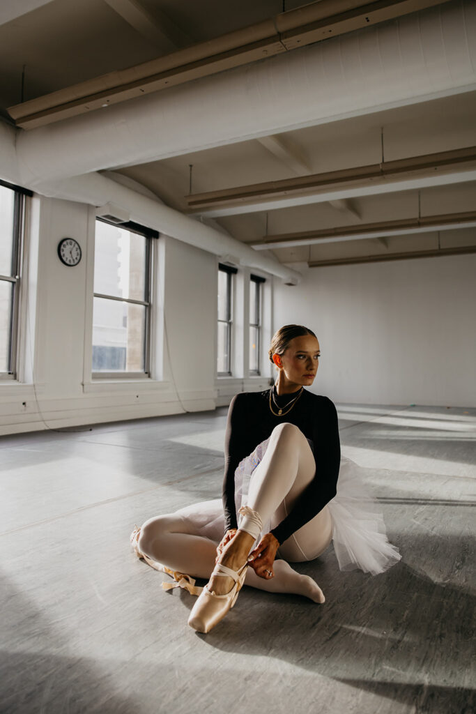 Lili Pfeifer of The Barbell Ballerina seated on studio floor in tutu and pointe shoes during fitness brand photography Minneapolis session