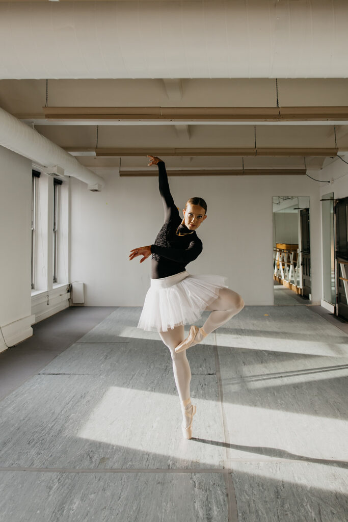 Lili Pfeifer of The Barbell Ballerina performing an arabesque in white tutu in dance studio during fitness brand photography Minneapolis session by Mycah Bain Photography