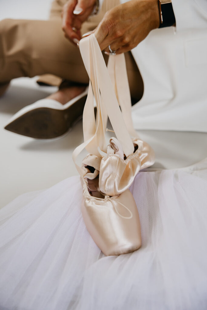 Close-up of pointe shoes being held over white tutu — branded B-roll detail from The Barbell Ballerina fitness brand photography Minneapolis session by Mycah Bain Photography