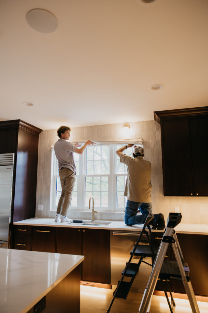 Bumble Bee Blinds installer standing on a kitchen counter installing a roller shade above a window during a Minneapolis home services brand photography session