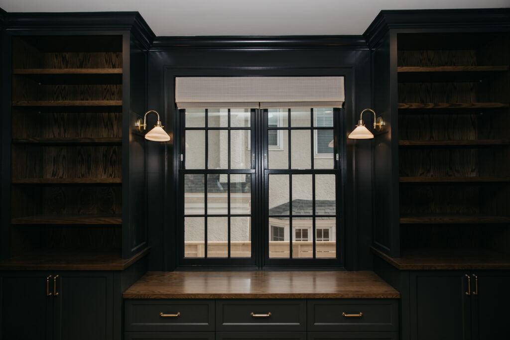 Wide shot of a built-in bookshelf nook with a roman shade and French doors in the background