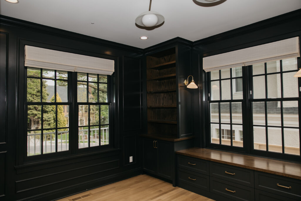 Custom roman shade in a dark built-in office nook with brass sconces and wood flooring