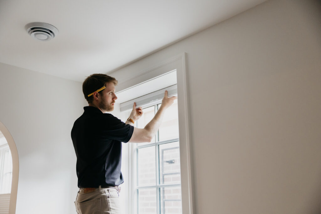 Installer adjusting hardware on a roman shade near the ceiling