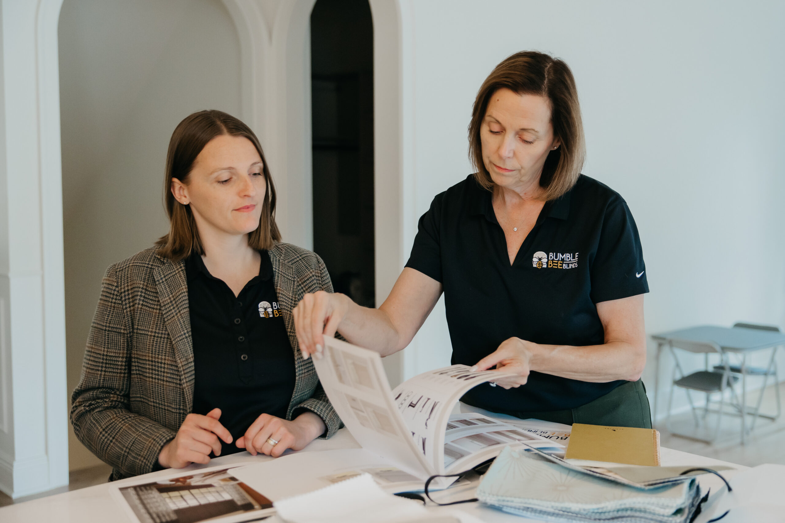 Brand photography for home services businesses Minneapolis — two Bumble Bee Blinds team members reviewing a window treatment sample book together