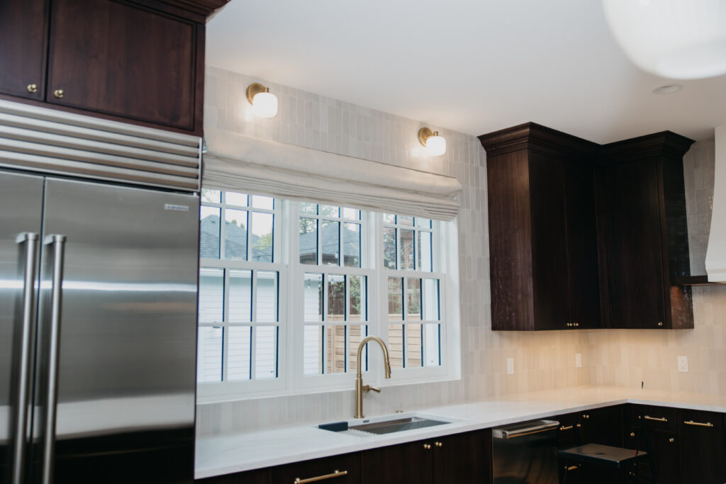 Roman shade installed above a kitchen window with stainless appliances and dark wood cabinetry