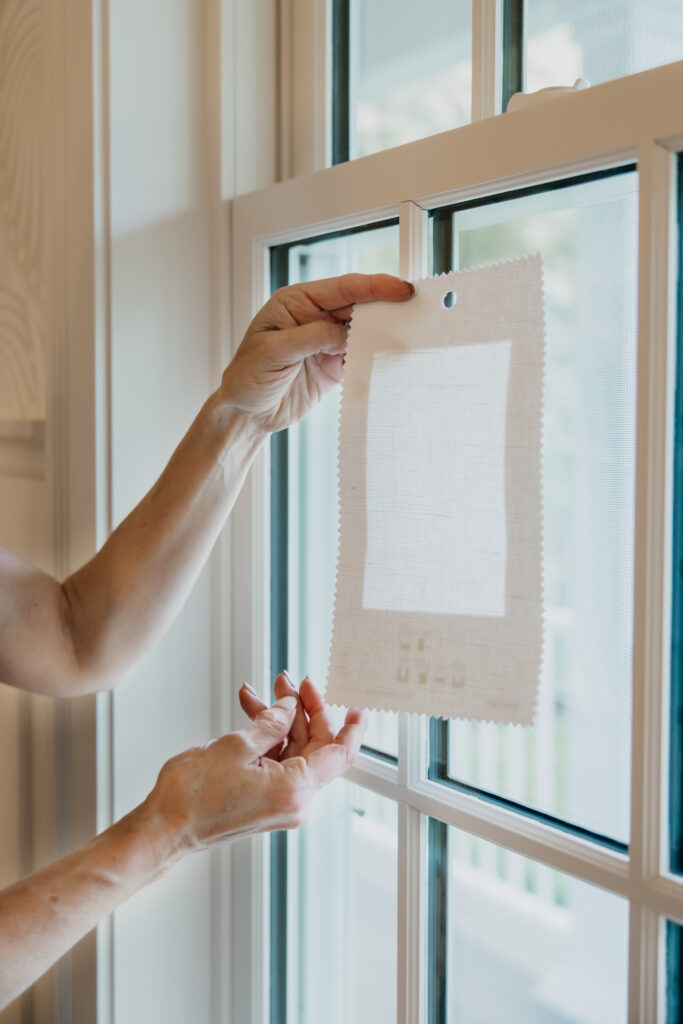 Hands holding a white fabric swatch sample up against a window to test light filtering
