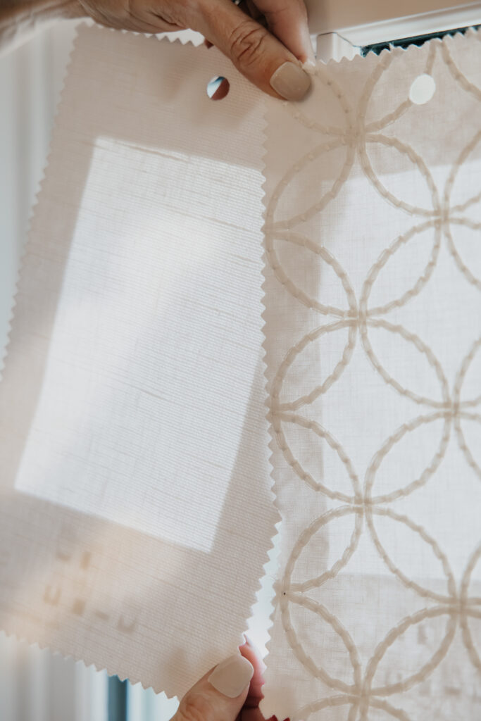 Hand holding a sheer geometric-pattern fabric swatch against natural window light