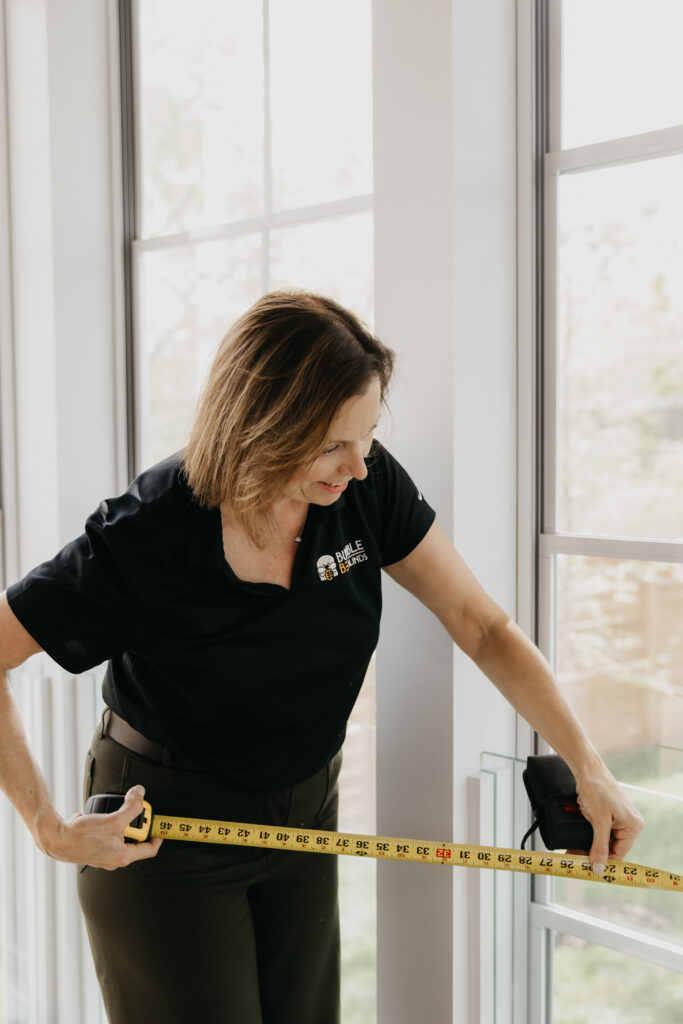 Bumble Bee Blinds design consultant measuring a window frame with a tape measure for a custom shutter installation