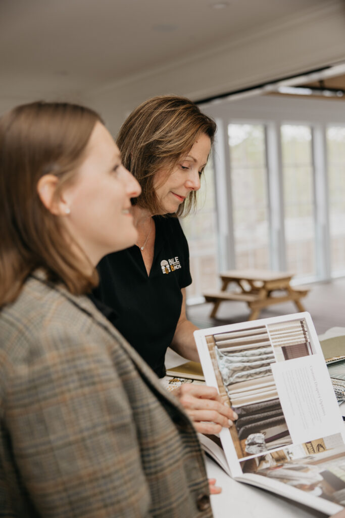 Two Bumble Bee Blinds team members smiling while reviewing a product catalog together