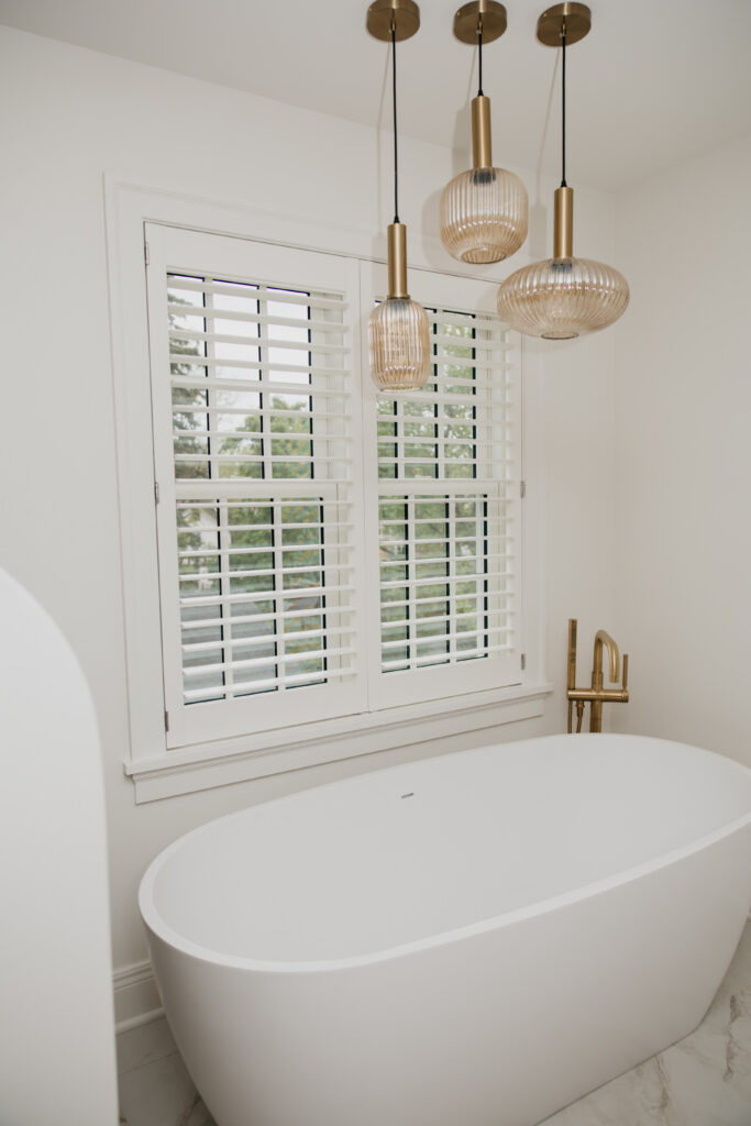Custom plantation shutters installed above a freestanding bathtub in a primary bathroom