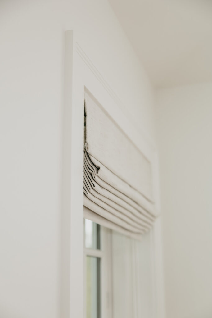 Close-up side angle of a roman shade mounted in a white window frame