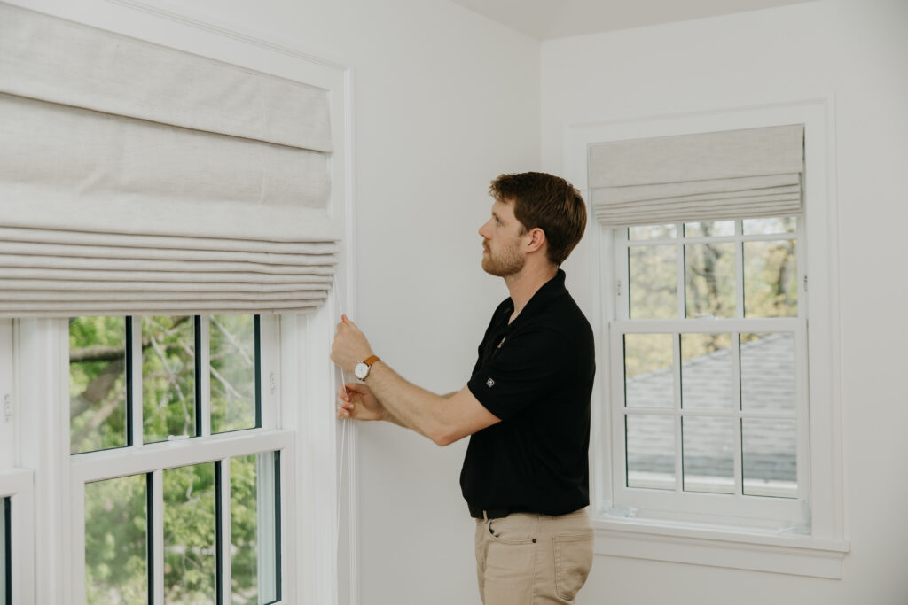 Bumble Bee Blinds installer adjusting a roman shade beside a window during installation