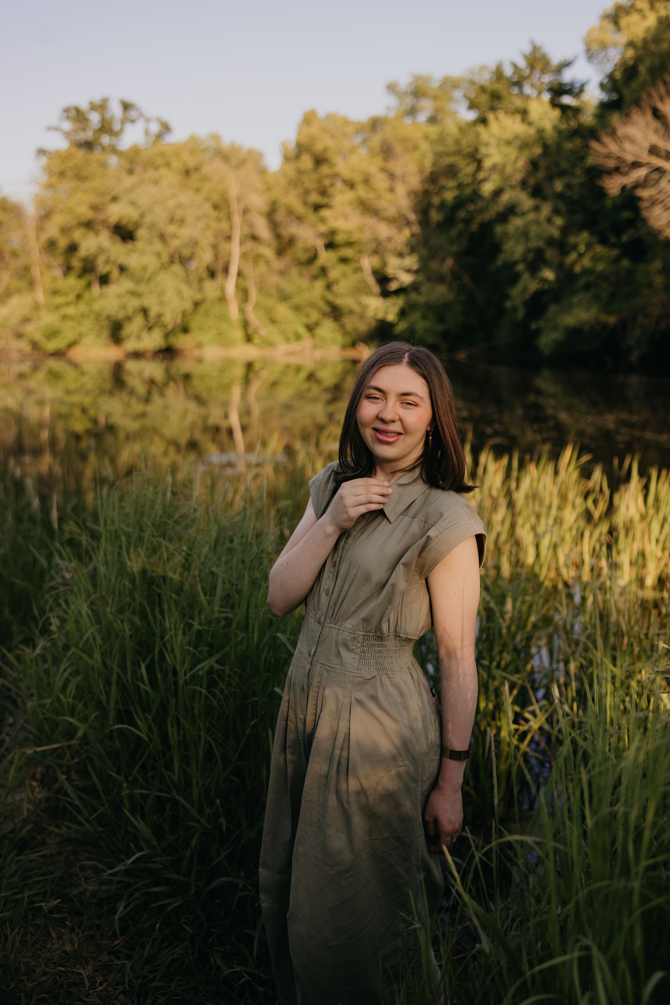 Saint Paul Academy senior in olive dress smiling by reflective pond at Longfellow Gardens golden hour
