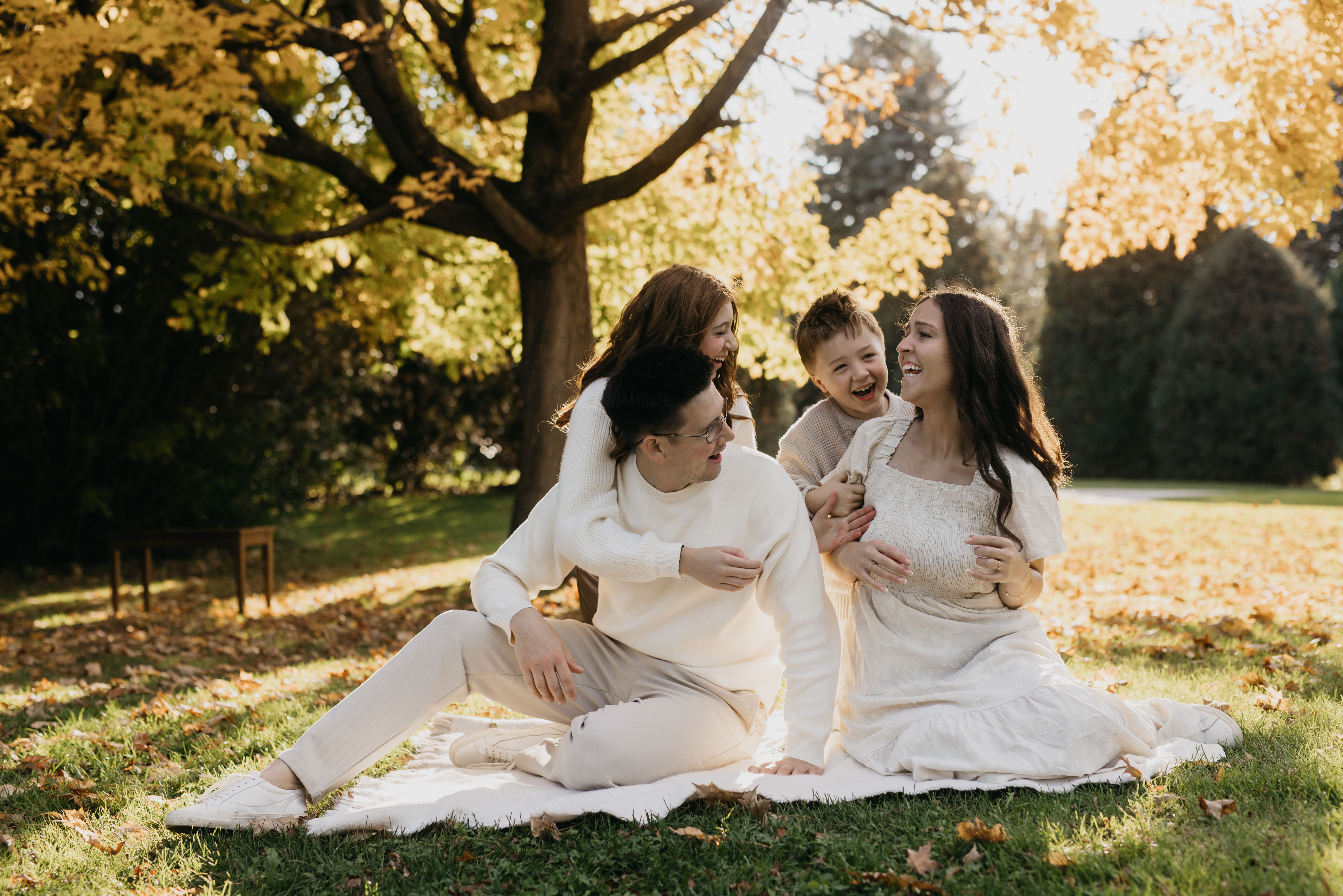 Family of four laughing together on a blanket in neutral tones family photos outfits under golden fall trees