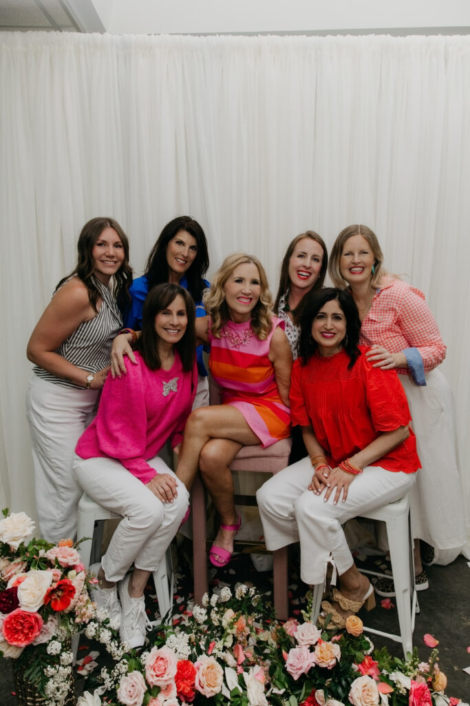 Full Haute House Studio team posing together in front of a white backdrop surrounded by lush floral arrangements during brand photography session