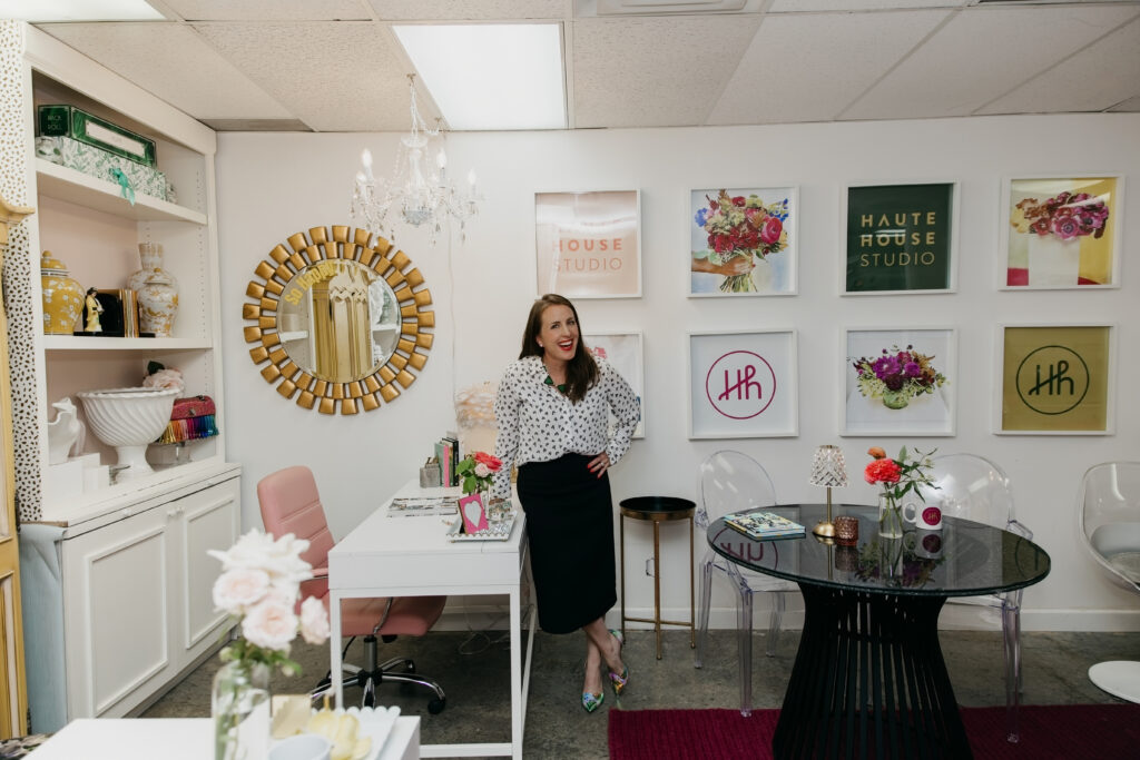 Haute House Studio team member in a polka dot top standing in the fully styled studio interior surrounded by branded artwork and floral decor