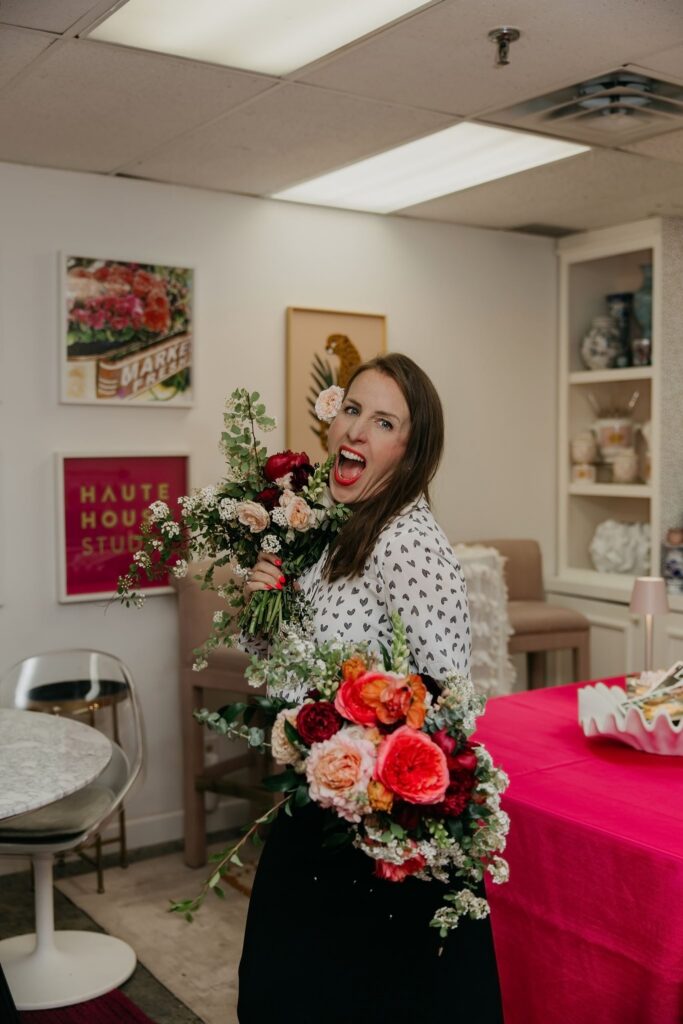 Haute House Studio team member in a polka dot top laughing and holding a large floral bouquet in the studio