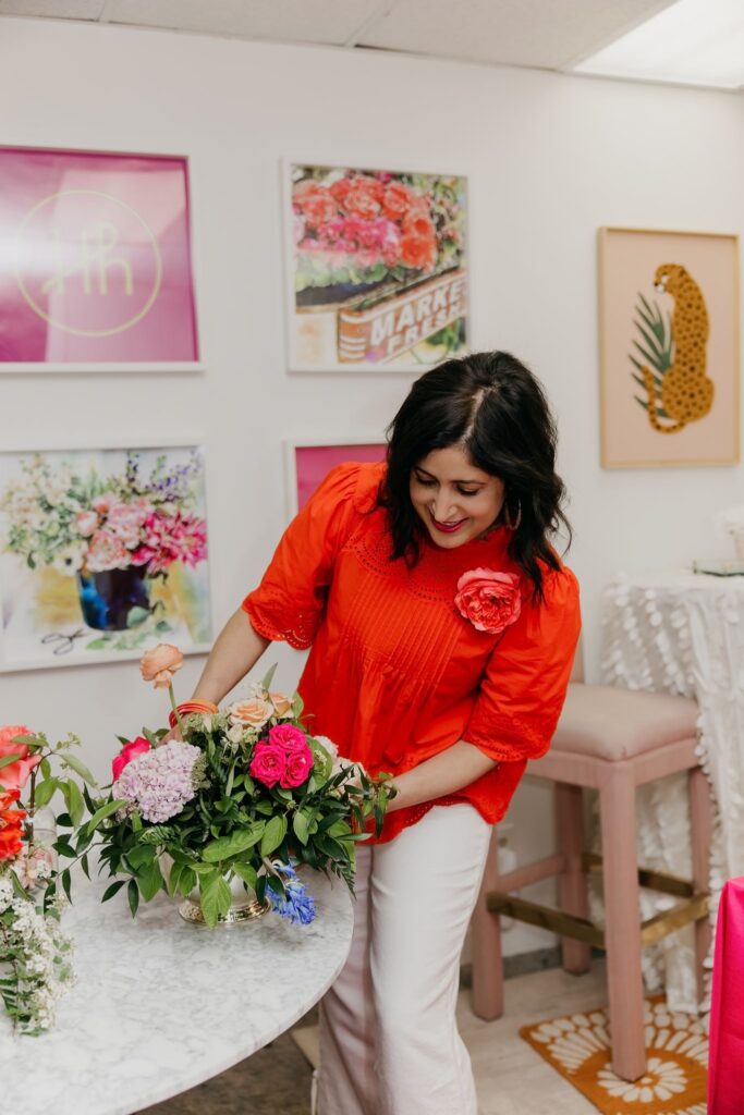Bridget Connell of Haute House Studio in an orange and pink striped dress arranging flowers on a white table in their Edina studio