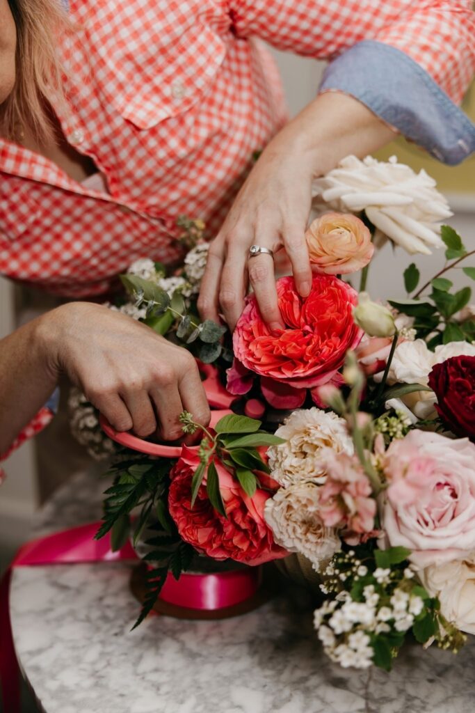 Close-up of hands arranging red coral and blush garden roses into a floral centerpiece during Haute House Studio brand session Minneapolis
