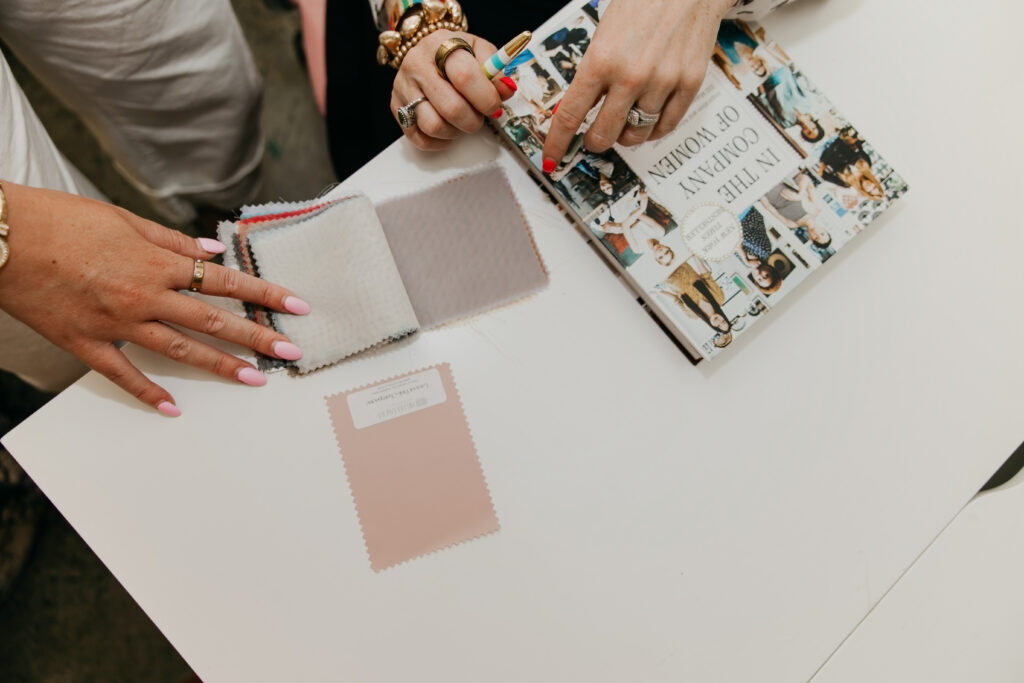 Close-up of hands reviewing color swatches and a floral inspiration book on a white table during Haute House Studio event design consultation