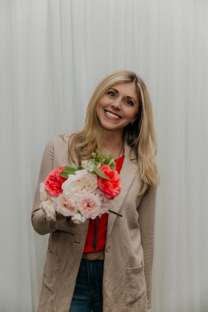Haute House Studio team member with blonde hair holding a blush and coral flower bouquet against a white backdrop during brand session