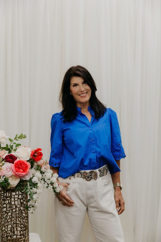 Haute House Studio team member in a cobalt blue shirt standing next to a floral arrangement against a white backdrop in Edina Minnesota