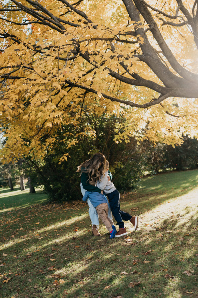 outdoor family photoshoot idea of a mom and dad spinning their son playfully under golden fall leaves