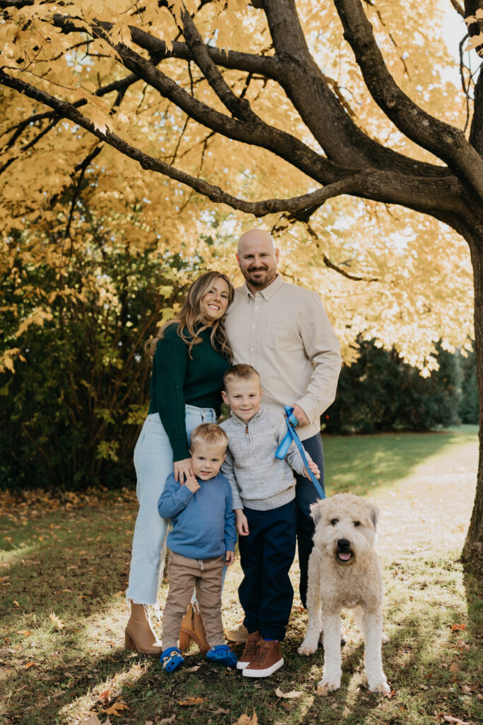 outdoor family photoshoot idea of a family of four and their dog standing together under golden fall tree branches