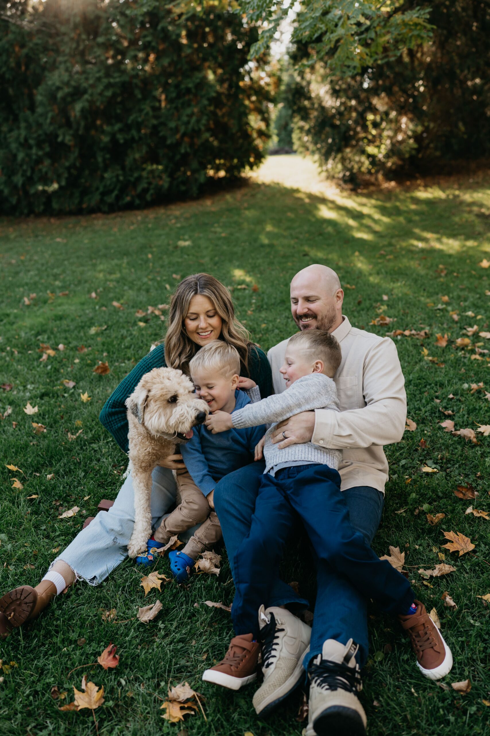 outdoor family photoshoot idea of parents and kids sitting in the grass laughing while their dog joins in