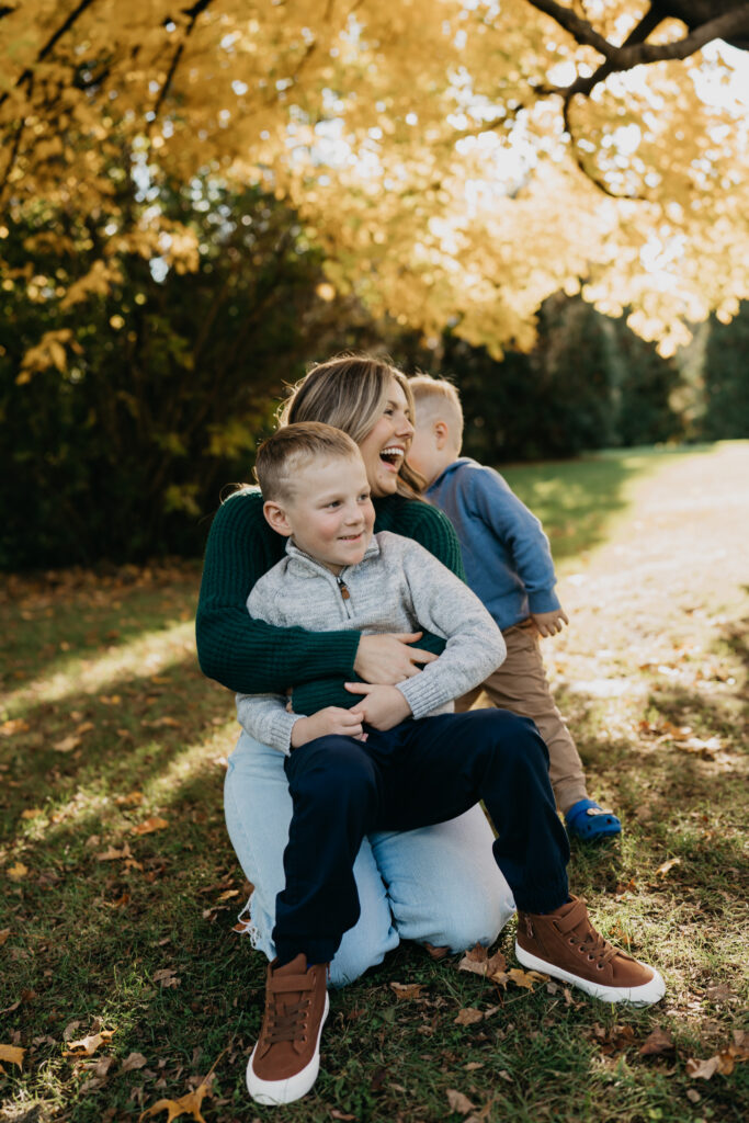 outdoor family photoshoot idea of a mom laughing while holding her two sons close under fall tree branches