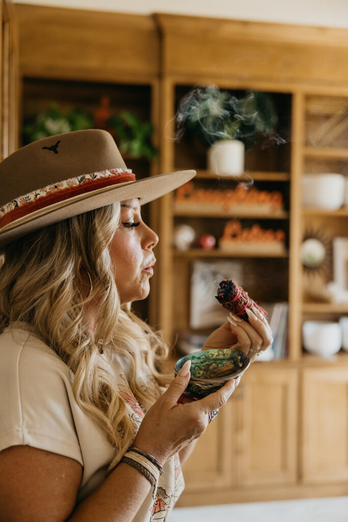 Close-up profile of women's wellness coach in wide-brim hat holding a small singing bowl with smoke during brand photography shoot