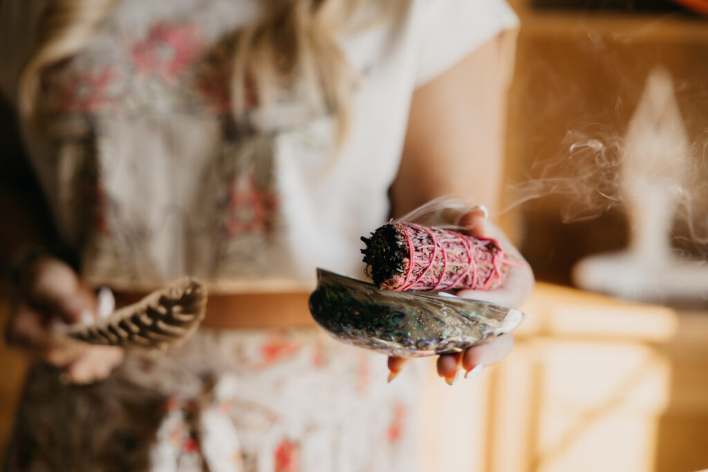 Close-up of hands holding a lit sage bundle on an abalone shell during women's wellness brand photo shoot