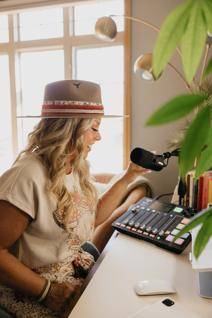 Women's mentor smiling while seated at her podcast desk surrounded by plants during Laughing Lotus brand shoot