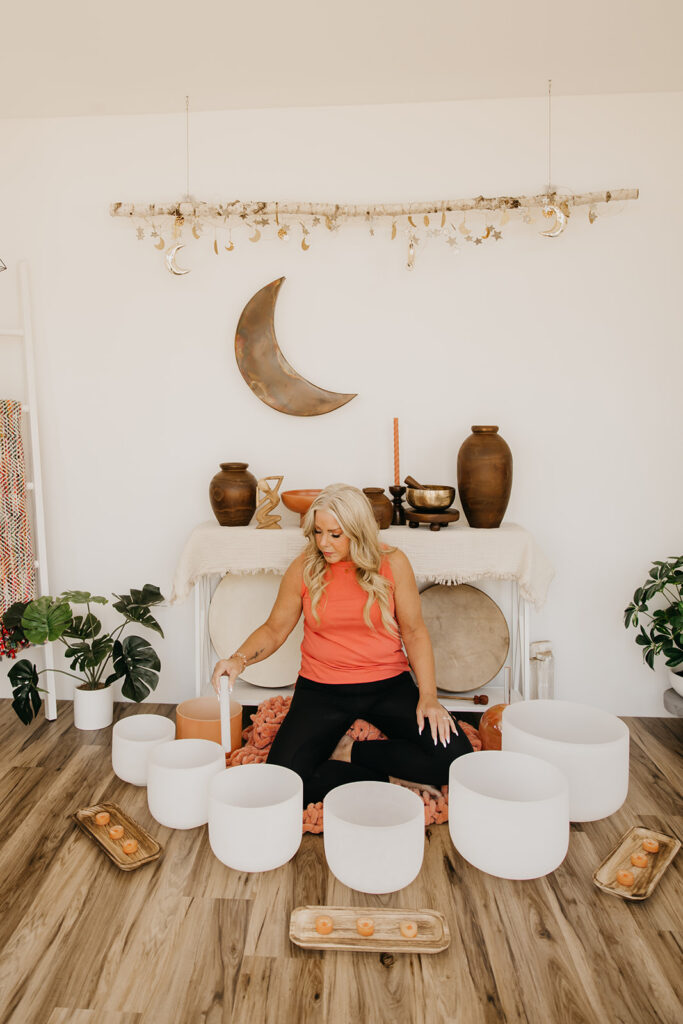 Women's energy healer with crystal singing bowls in front of crescent moon wall decor during brand photography session