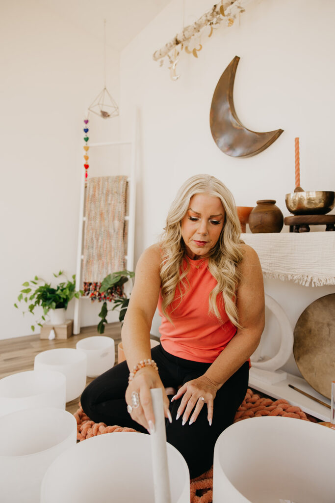 Women's mentor sitting cross-legged beside crystal singing bowls during sound healing brand photo shoot