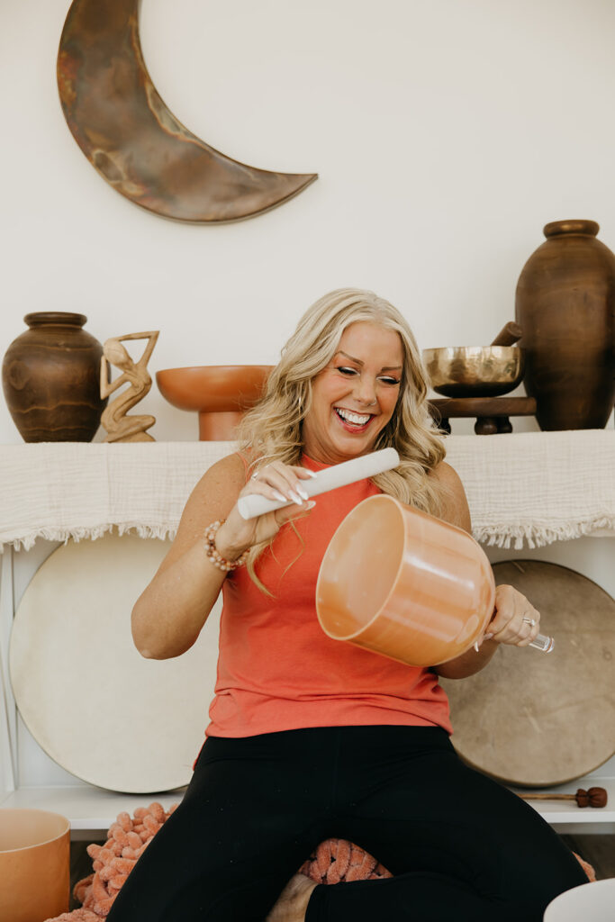Women's wellness coach laughing while holding a large copper bowl in her sound healing studio during brand photography session