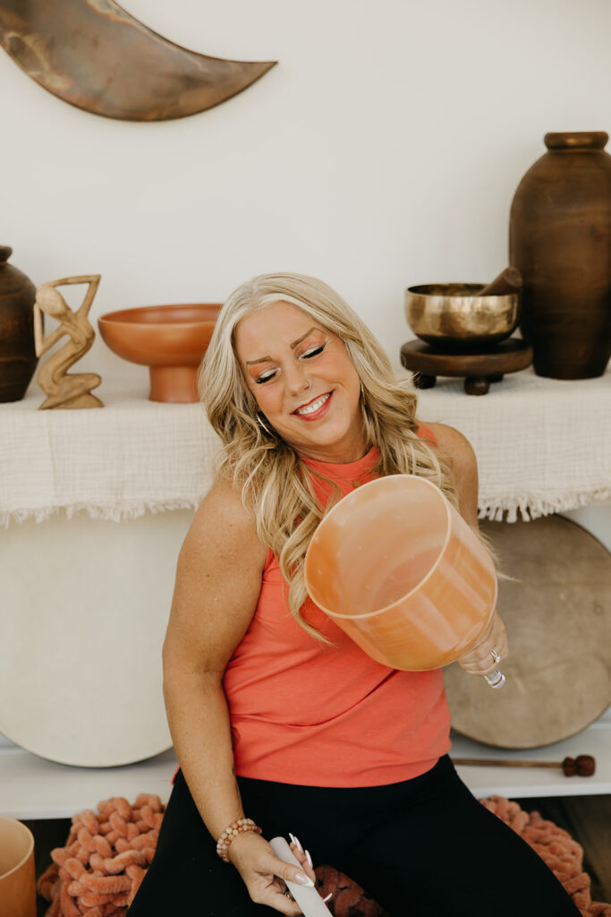 Women's energy healer smiling and dancing with a copper singing bowl in front of boho altar decor during brand shoot
